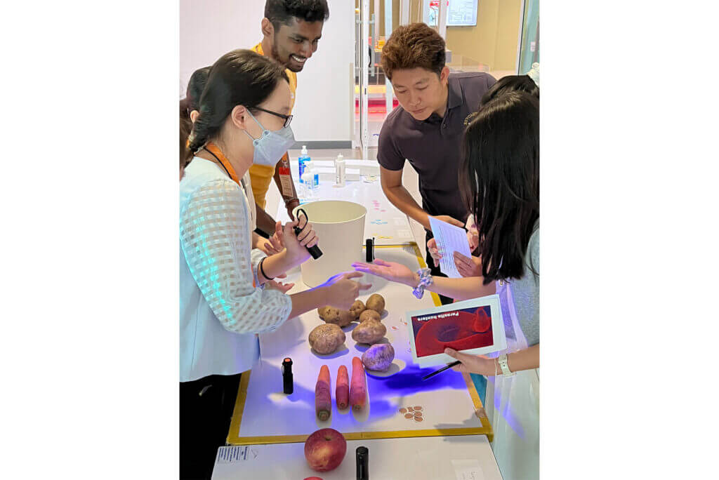 Researcher, on left, holding a UV torch and shining it on the hand of a student, as part of a pathogen transmission demonstration.
